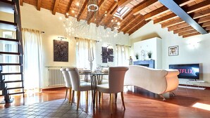 A spacious living room with a modern chandelier, wooden ceiling beams, a white sofa, and a flat-screen TV displaying 'Netflix'. - Atlas Apartments  (Bergamo)