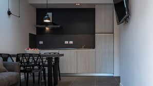 A modern kitchen with dark cabinetry, a dining area with a table and chairs, and a flat-screen TV mounted on the wall. - Astoria Boutique Apartments (Bologna)