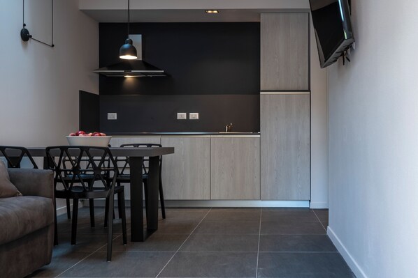 A modern kitchen with dark cabinetry, a dining area with a table and chairs, and a flat-screen TV mounted on the wall.