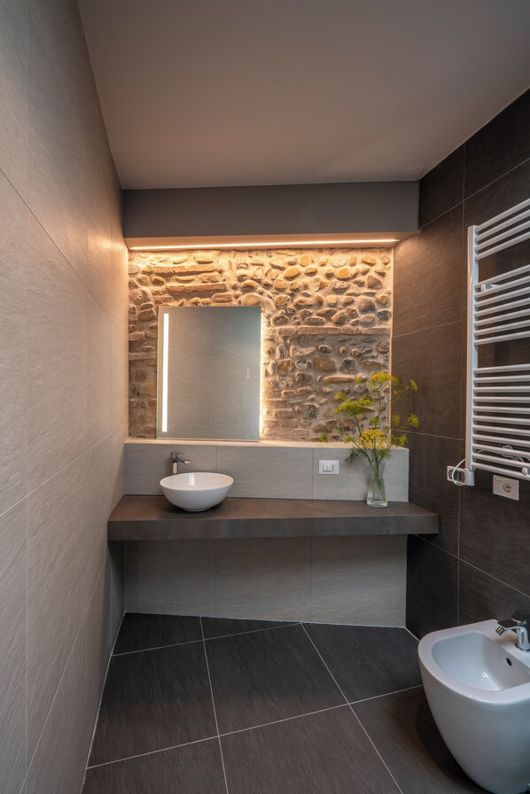 Un baño moderno con una pared de acento de piedra, un lavabo blanco y un bidé.