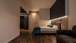 A modern bedroom with a bed, a dark sofa, and a wooden floor. - Astoria Boutique Apartments (Bologna)