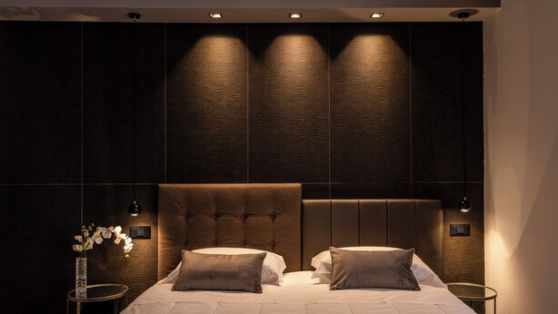 A modern bedroom with a large bed, two bedside tables, and a wall-mounted light fixture. - Astoria Boutique Apartments (Bologna)