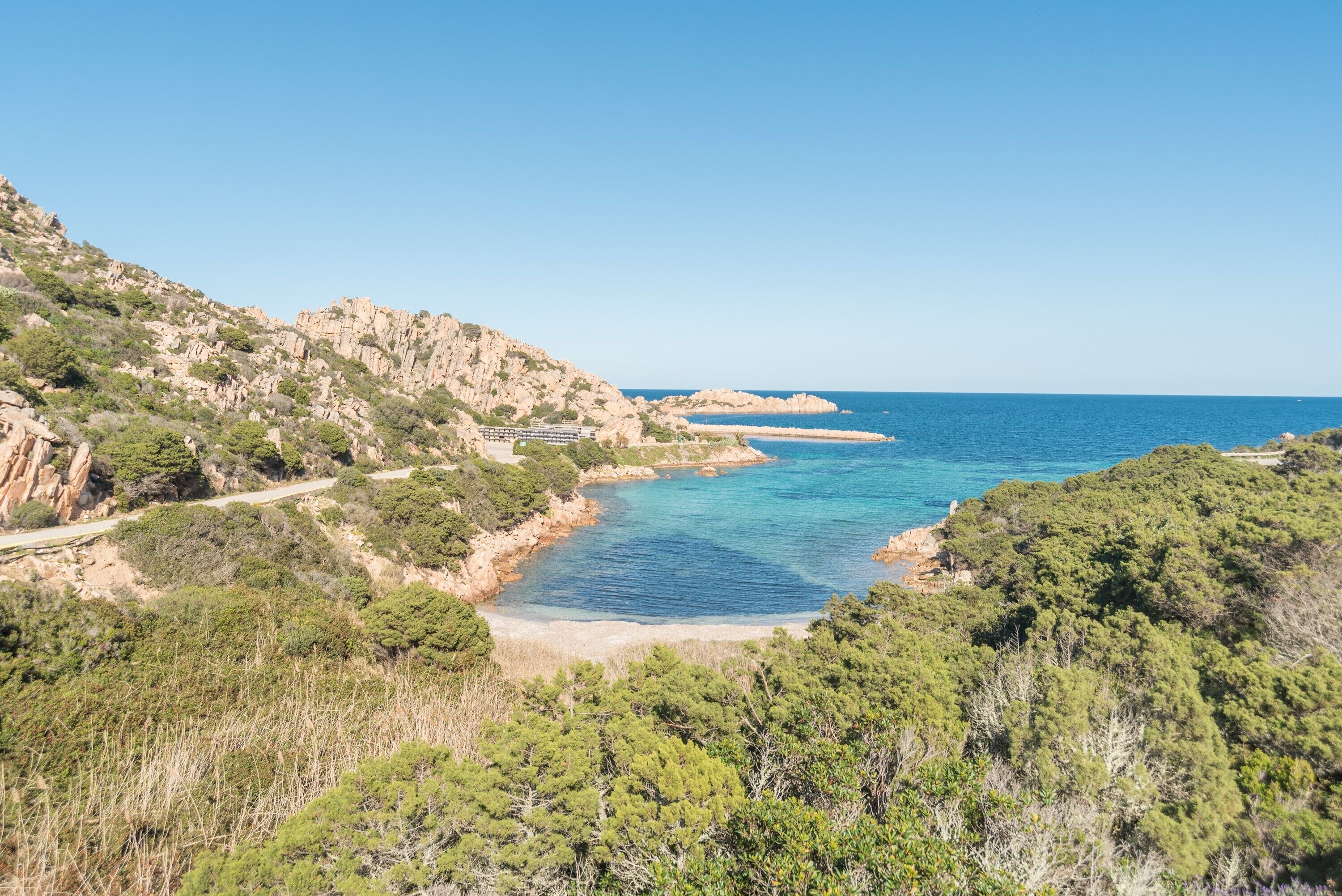 Paesaggio costiero con una strada, terreno roccioso e una spiaggia.