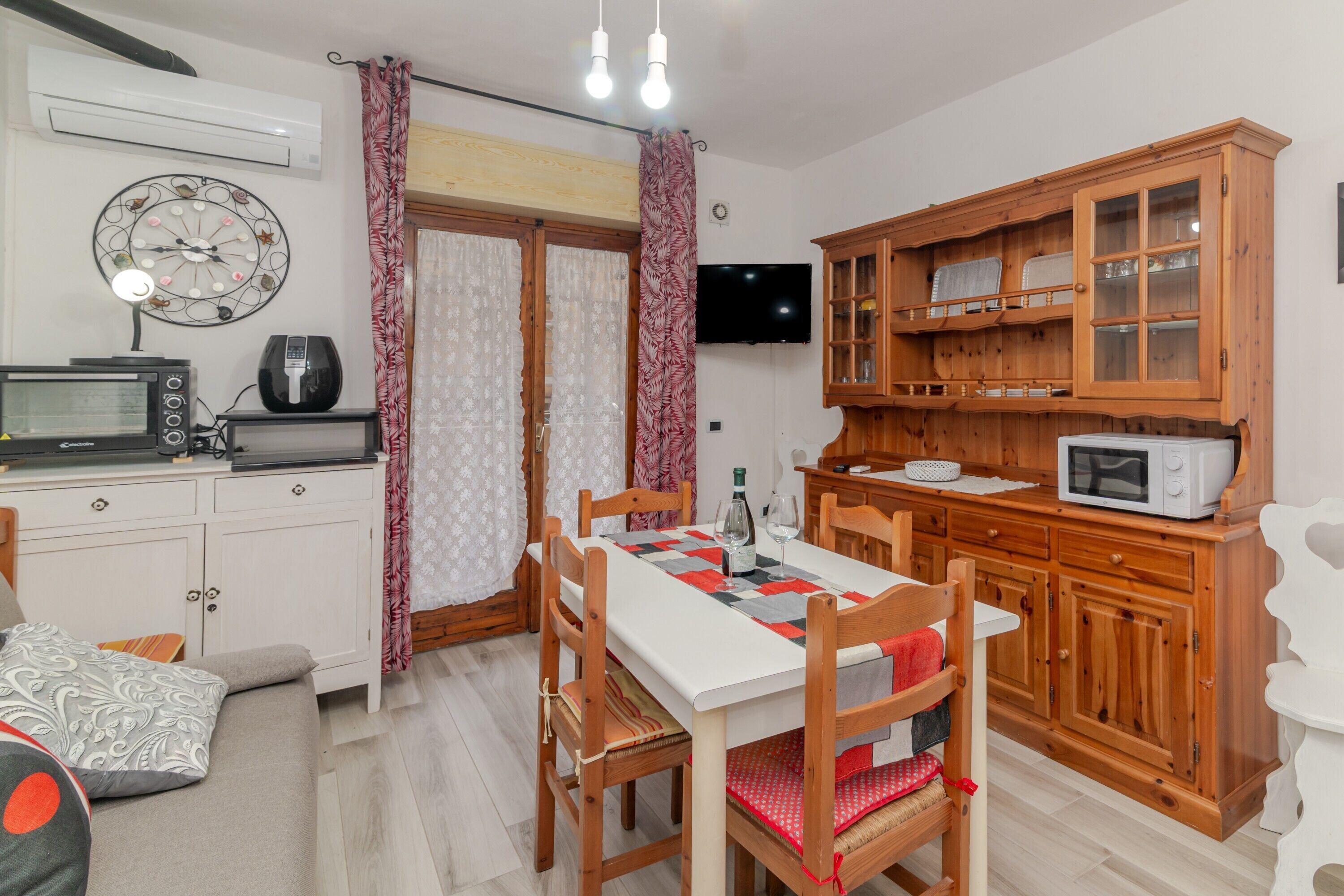 Une cuisine compacte comprenant une table à manger, des chaises, un four à micro-ondes, un téléviseur et un meuble en bois doté de portes en verre.