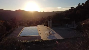 Piscina rectangular con muelle de madera y sillas de descanso, rodeada de colinas y un cielo despejado.