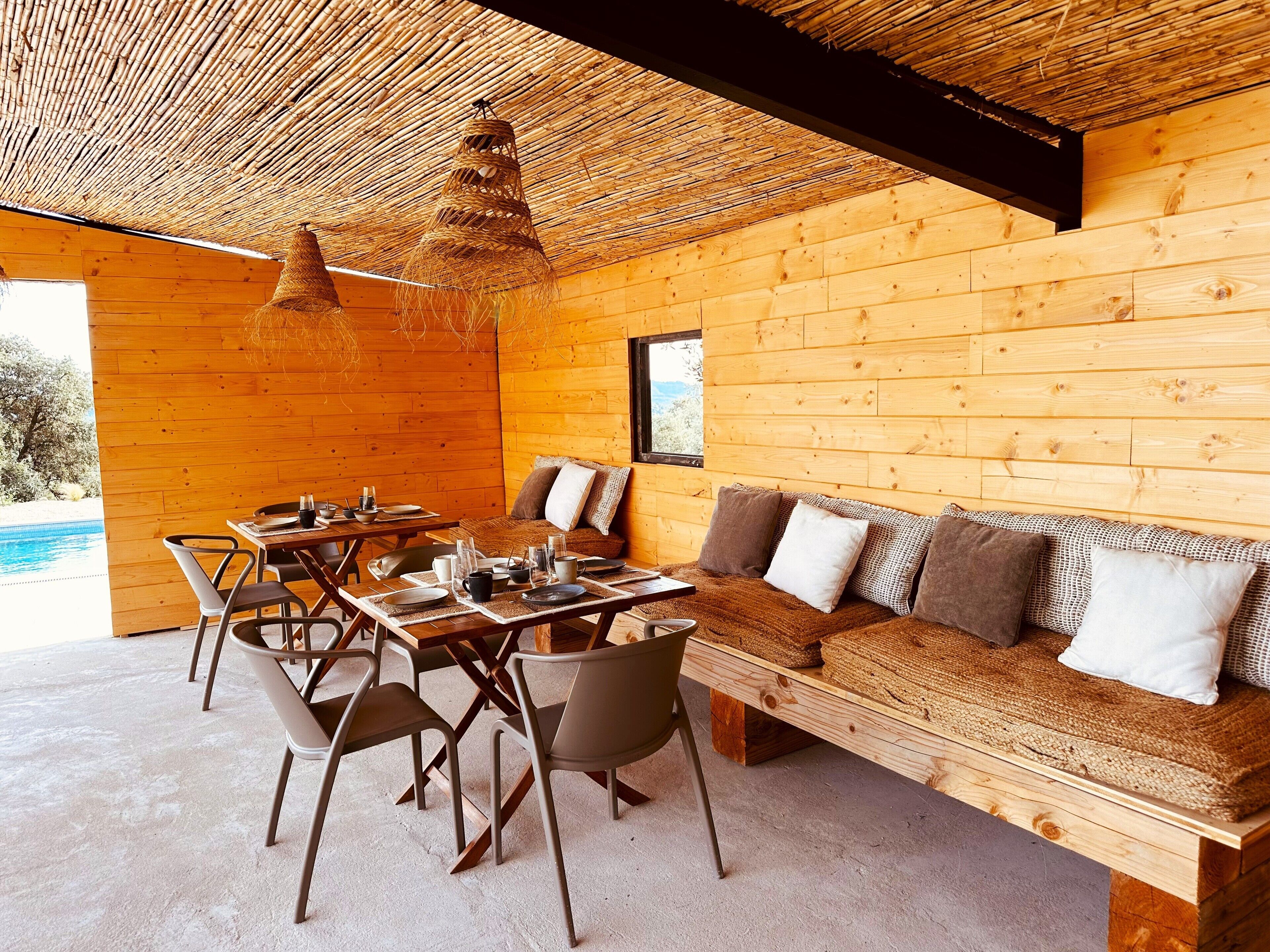 Una cabaña de madera con comedor, sofá y vistas a una piscina.