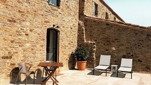 A stone building with a tiled roof, a small door, and a window. There are outdoor chairs and a table. - Mimosa Lodge (Quart)
