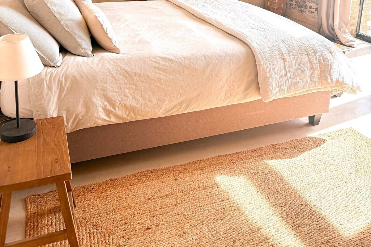 A bedroom with a bed, bedside table, lamp, and a mirror.