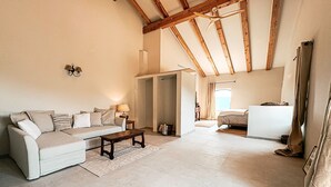 A spacious living room with a high ceiling, a sofa, a coffee table, and a bed in the background. - Mimosa Lodge (Quart)