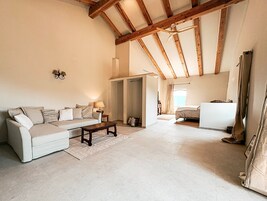 Uma sala de estar ampla, com teto alto, um sofá, uma mesa de centro e uma cama ao fundo.