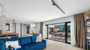 Ein modernes Wohnzimmer mit einem blauen Sofa, einem Essbereich und Blick auf eine Berglandschaft durch große Glastüren.