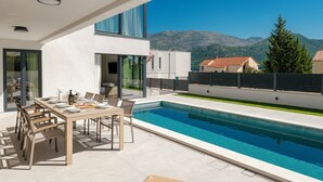 Ein zeitgenössischer Essbereich im Freien mit Pool, einem Tisch für vier Personen und Bergblick.