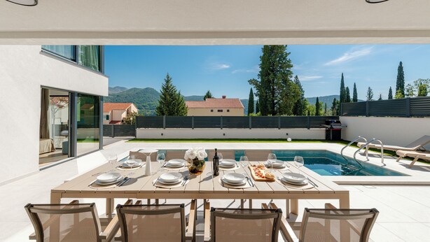 Ein Essbereich im Freien mit Pool, Tischen für vier Personen und Blick auf Berge und Bäume.