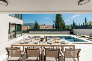 An outdoor dining area with a pool, tables set for four, and a view of mountains and trees. - Villa Rafela Delux Dubrovnik (Slano)