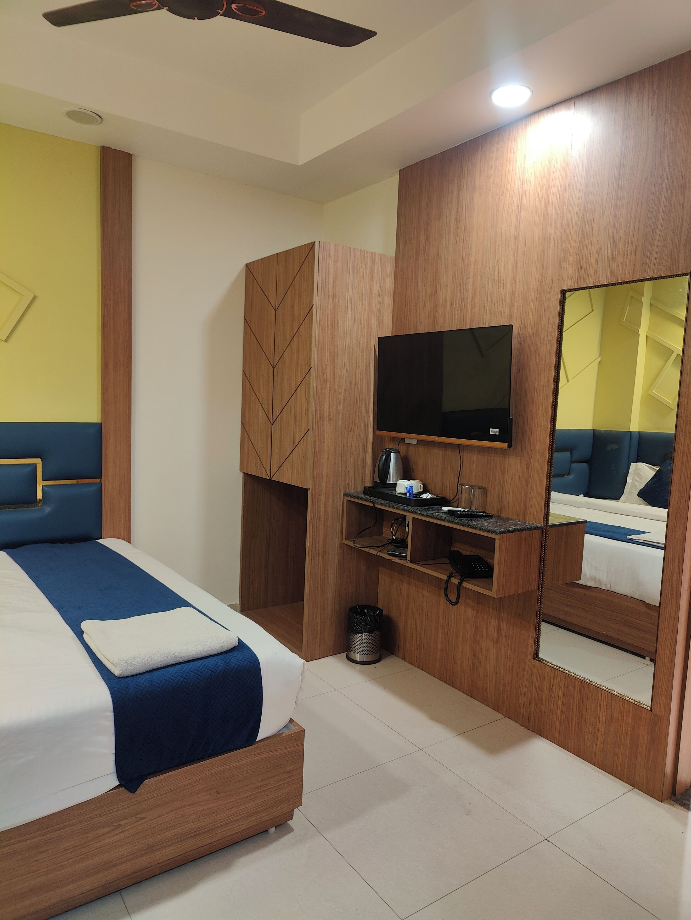 A hotel room with a bed, a TV, a mirror, and a ceiling fan.