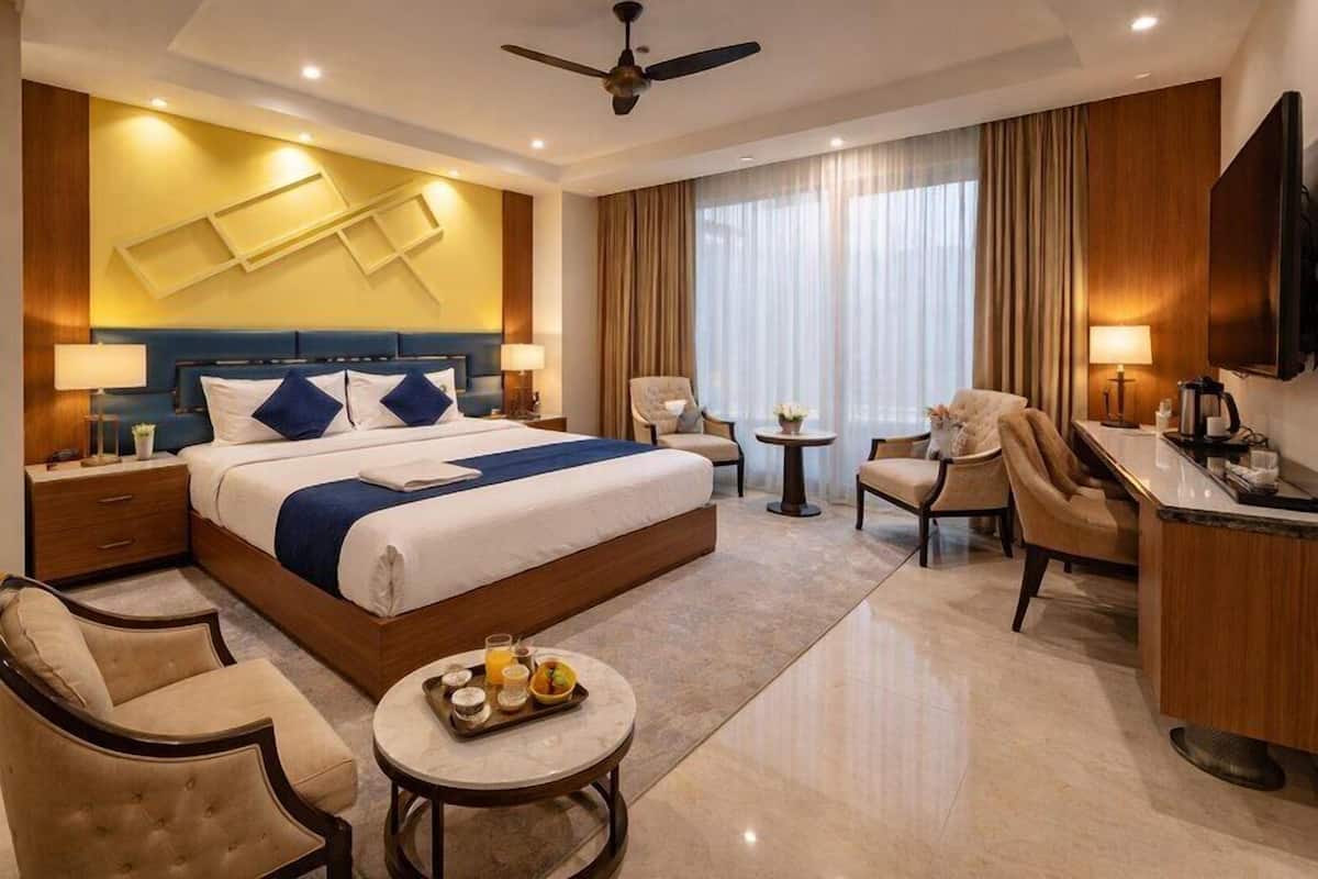 Une chambre d’hôtel avec un grand lit, deux fauteuils, un bureau, une télévision et un ventilateur de plafond.