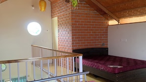 Une pièce avec un plafond en pente, un mur en briques et un lit doté d’un matelas rose.