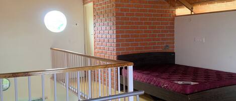 Una habitación con techo inclinado, pared de ladrillo y cama con colchón rosa.