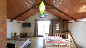 Une pièce avec un plafond en pente, un lit, une petite table avec un vase, un téléviseur fixé au mur et un balcon avec une balustrade.