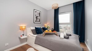 Moderni hotellihuone, jossa on sänky, yöpöytä, lamppu ja näkymä kaupunkiin.