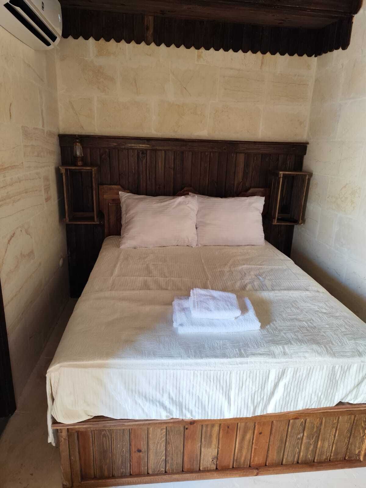 Una cama individual con cabecera de madera, dos mesitas de noche y una colcha blanca.