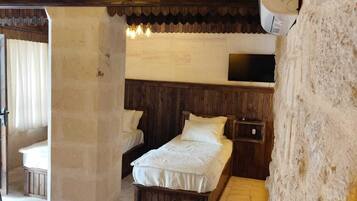 Una habitación rústica con paredes de madera y una cama con ropa de cama blanca. Hay una mesita pequeña con una tetera y una taza, y un televisor montado en la pared.
