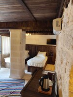 Una habitación rústica con paredes de madera y una cama con ropa de cama blanca. Hay una mesita pequeña con una tetera y una taza, y un televisor montado en la pared.