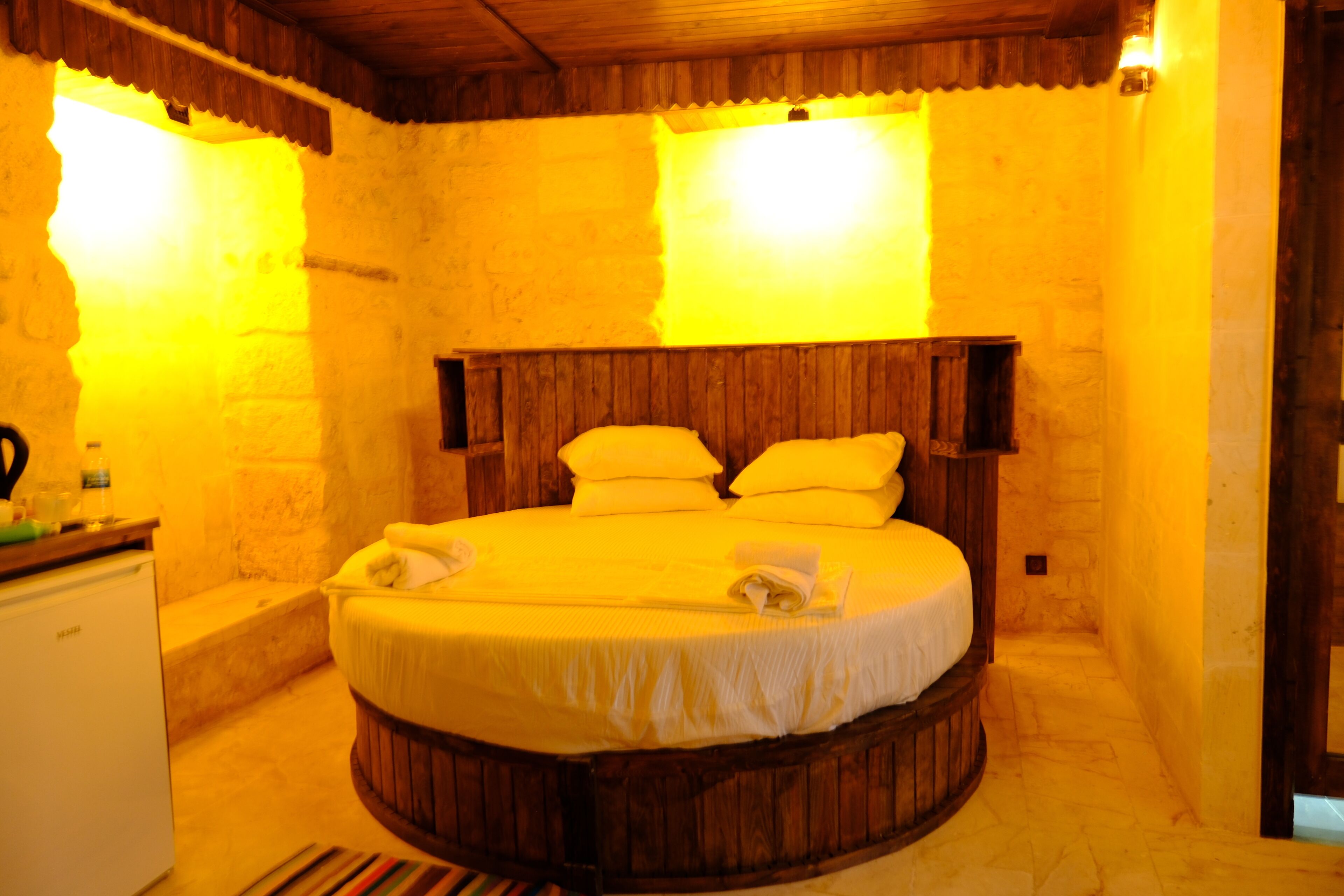 A circular wooden bed with white bedding in a room with stone walls and wooden ceiling.