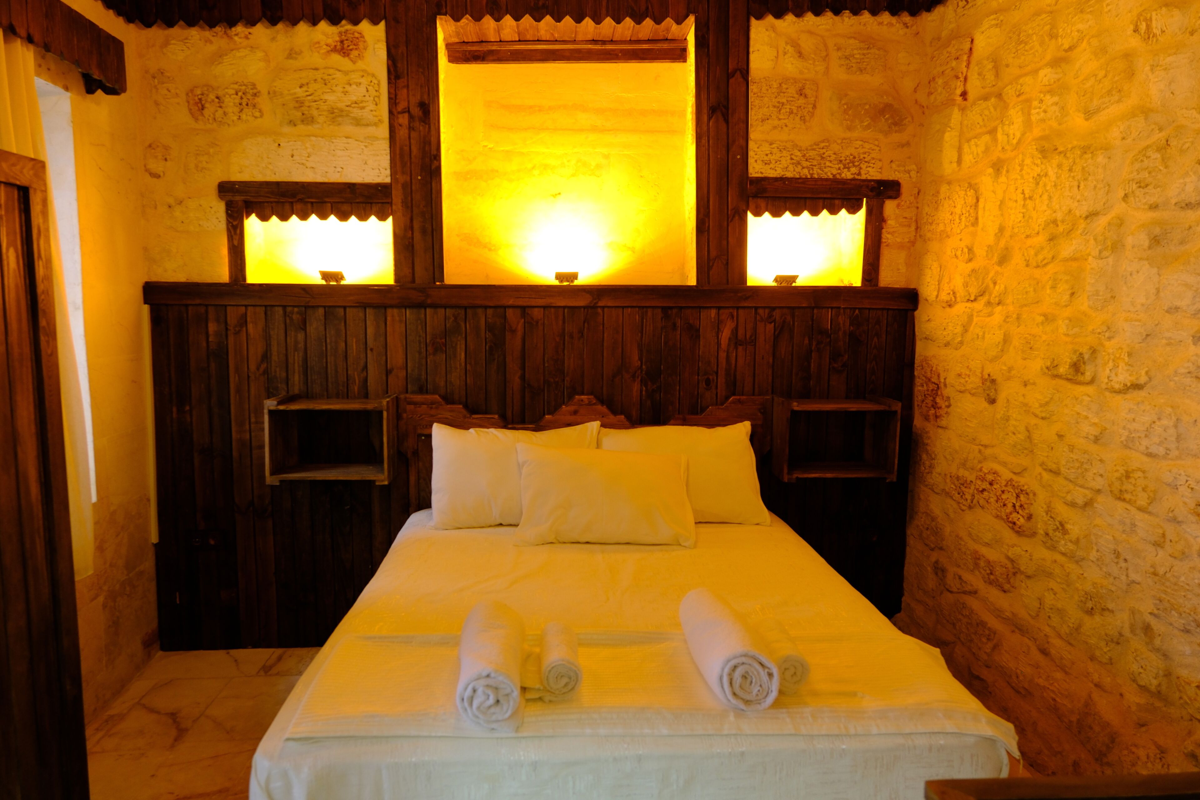 A room with a wooden headboard, a bed with white linens, and two bedside tables with lamps.