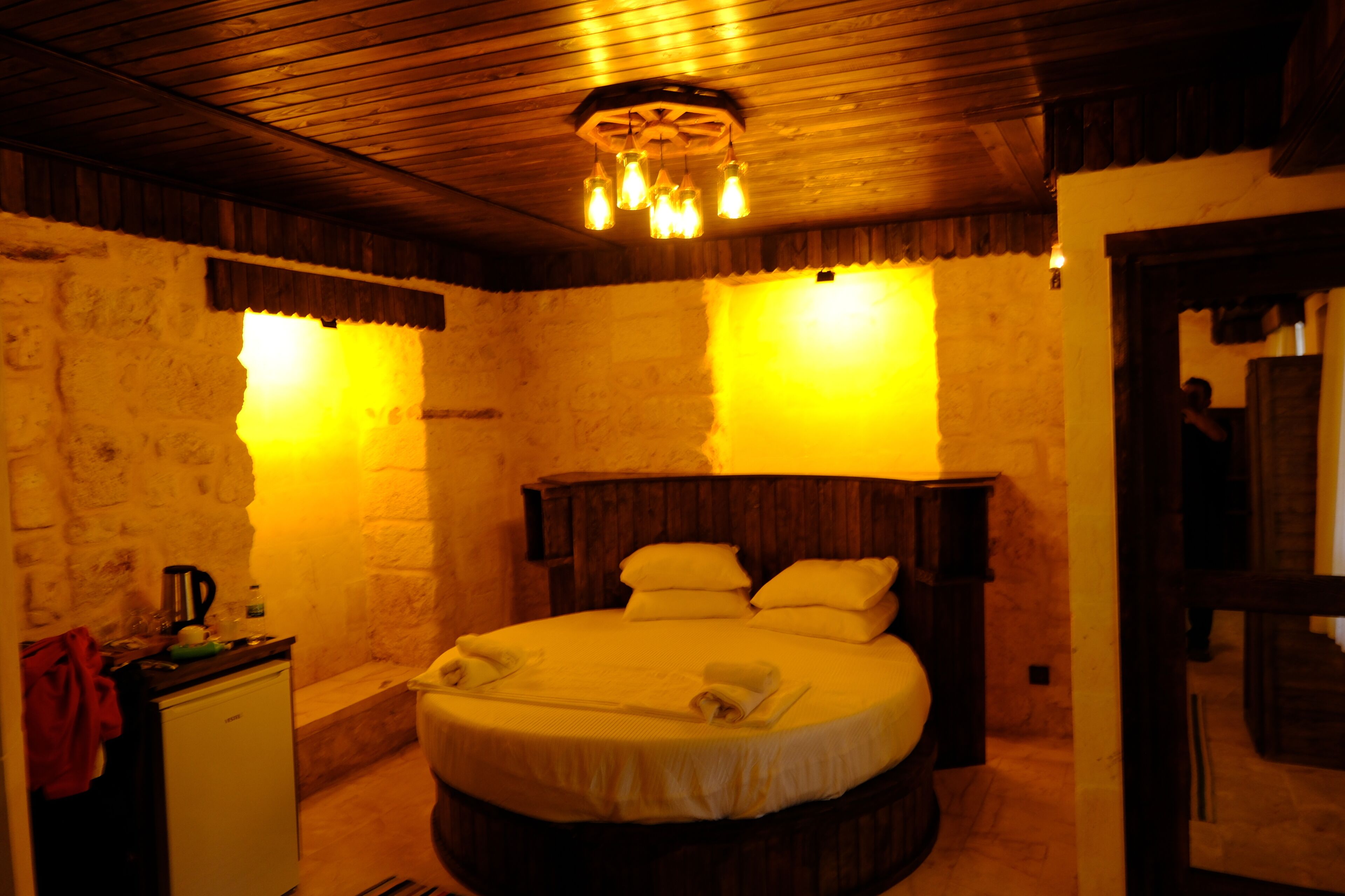 Una habitación acogedora con una cama redonda, techo de madera y pared de piedra.