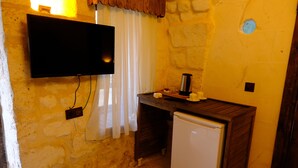 A compact kitchen with a TV mounted on the wall, a small refrigerator, and a wooden counter with a coffee maker. - SUMATRA OTEL (Şanlıurfa)