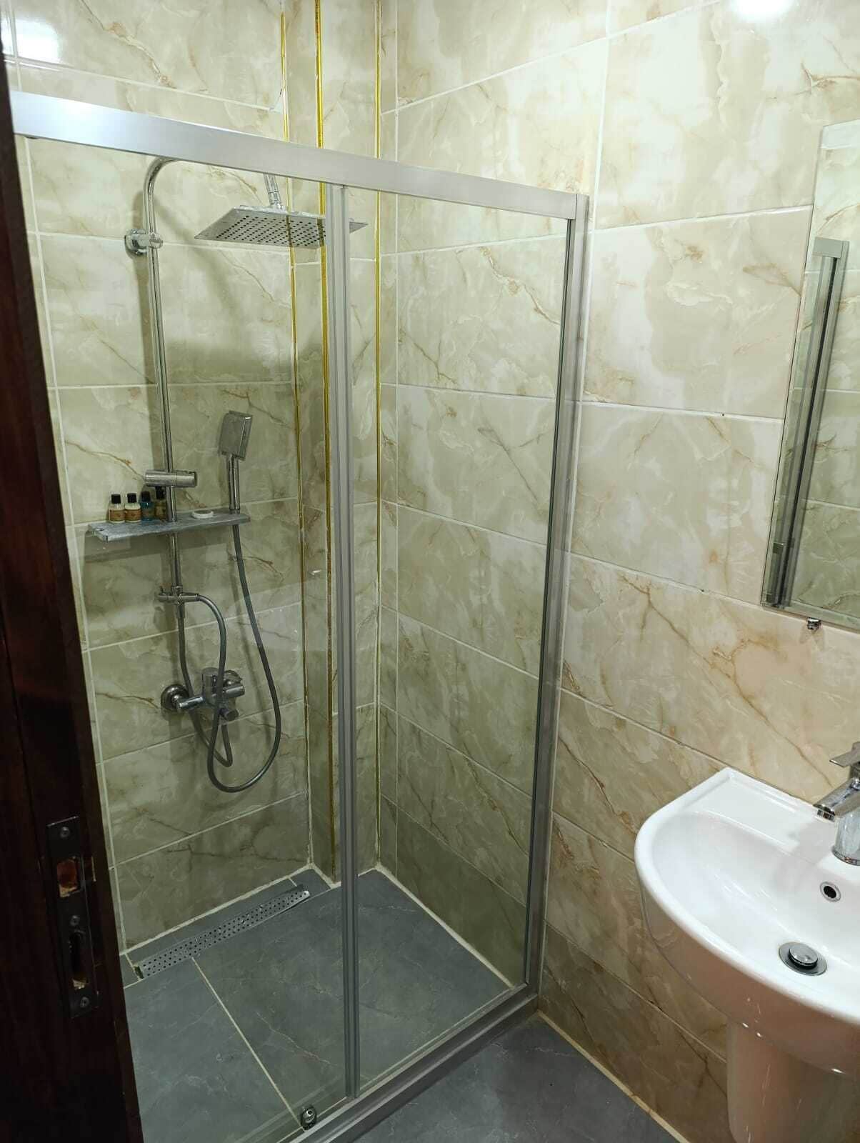 Un box de ducha con paredes de vidrio, un cabezal de ducha de mano y un grifo empotrado.