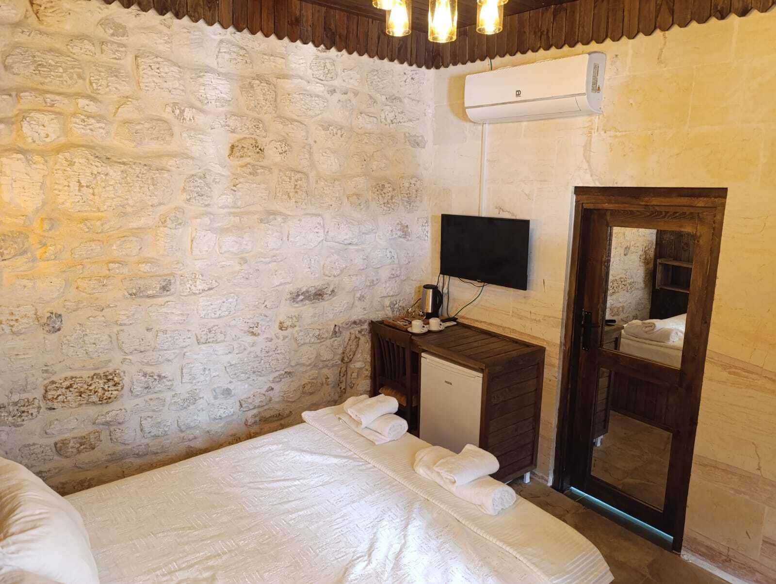 Een slaapkamer met een stenen muur, een houten nachtkastje met een televisie, een klein kastje en een bed met handdoeken.