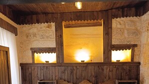 A bedroom with a wooden headboard, two bedside tables with lamps, a bed with white linens, and a stone wall. - SUMATRA OTEL (Şanlıurfa)