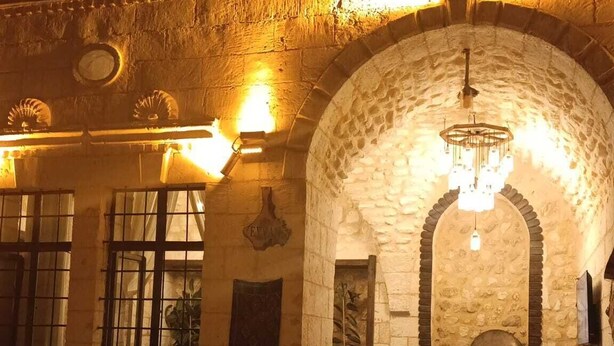 An outdoor courtyard with stone walls, a wooden bench, and a chair. - SUMATRA OTEL (Şanlıurfa)