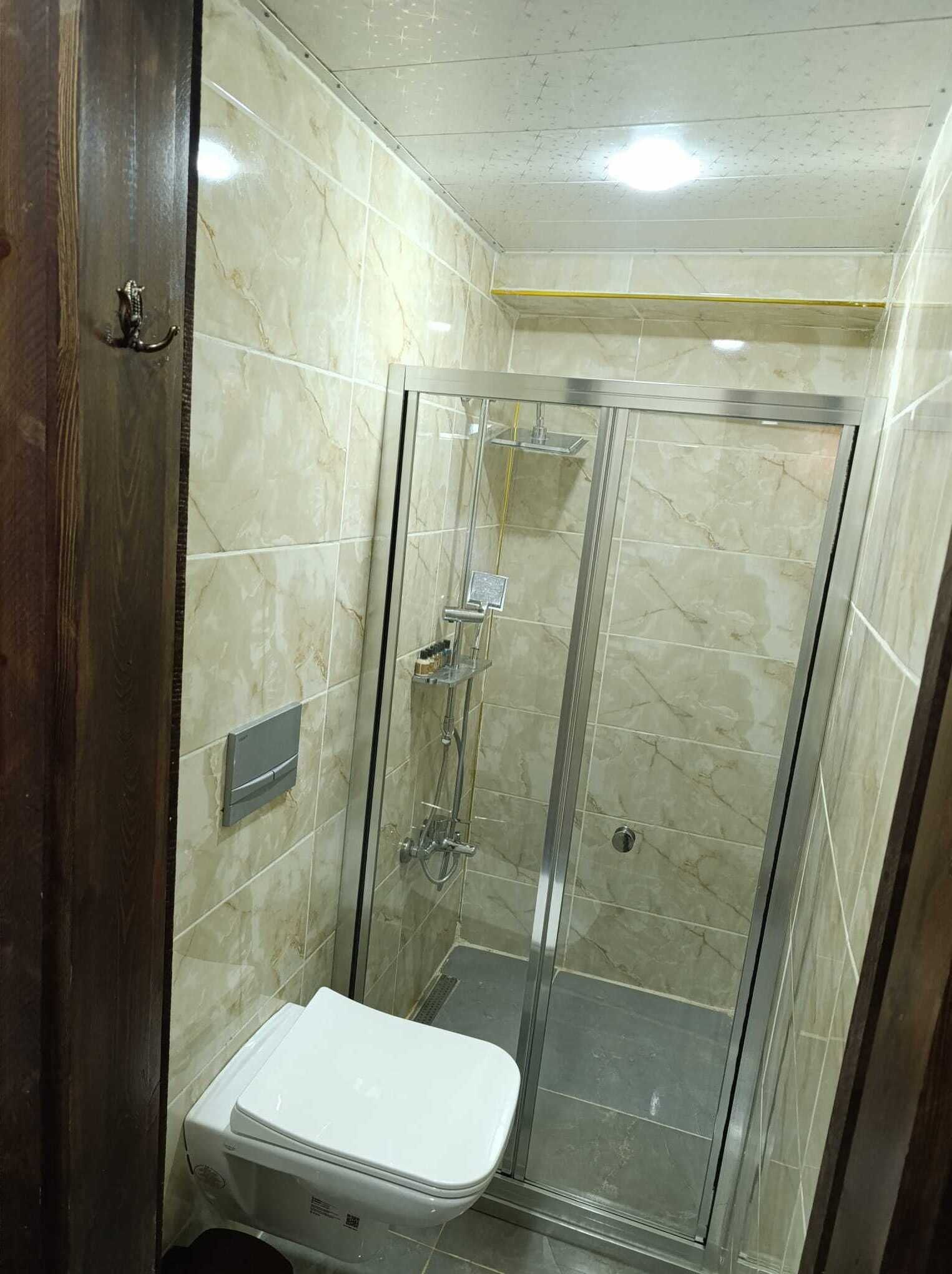 Un baño con cabina de ducha de vidrio, inodoro y pared con azulejos de mármol.