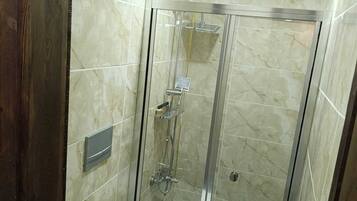 Un baño con cabina de ducha de vidrio, inodoro y pared con azulejos de mármol.