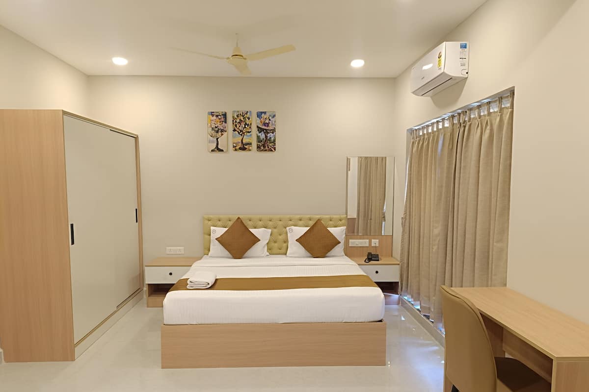 Habitación de hotel con cama, mesita de noche, escritorio, armario, ventilador de techo, aire acondicionado y tres cuadros colgados en la pared.