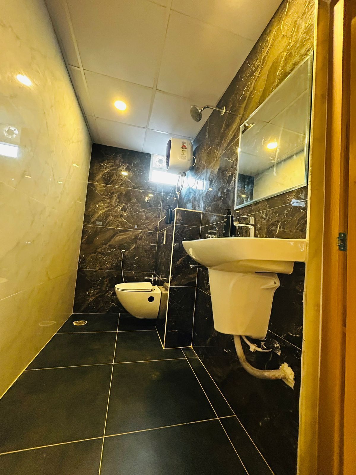 Un baño moderno con inodoro, bidé y lavamanos, con paredes de mármol oscuro y baldosas negras.