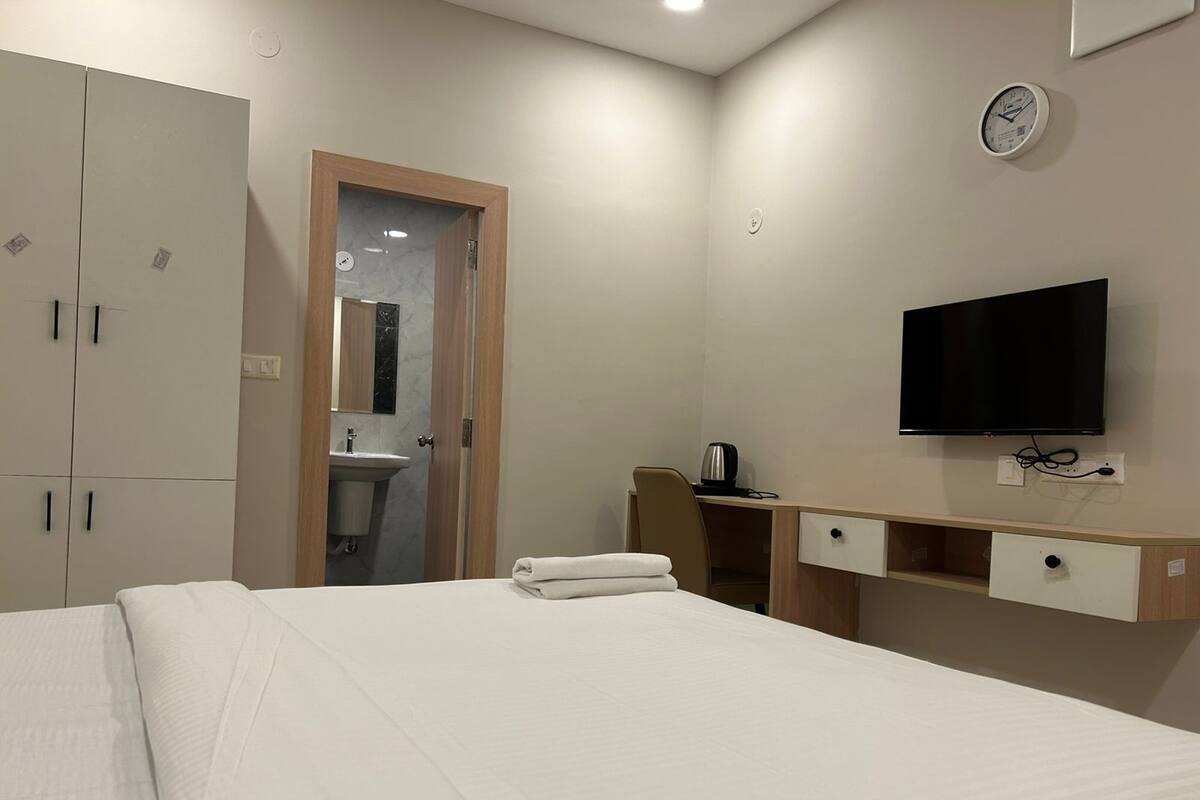 Habitación de hotel con cama, televisor, escritorio con tetera y armario.