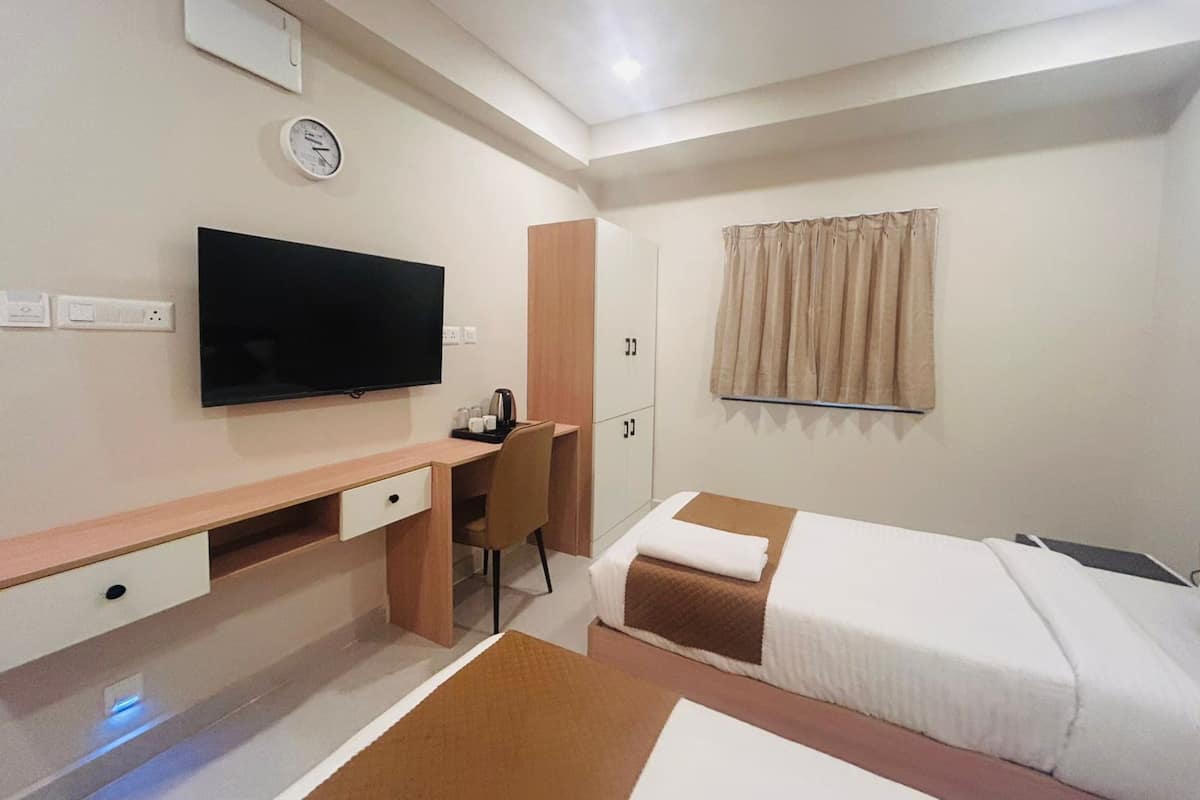 Habitación de hotel con cama, escritorio, silla, televisor, reloj y ventana con cortinas.