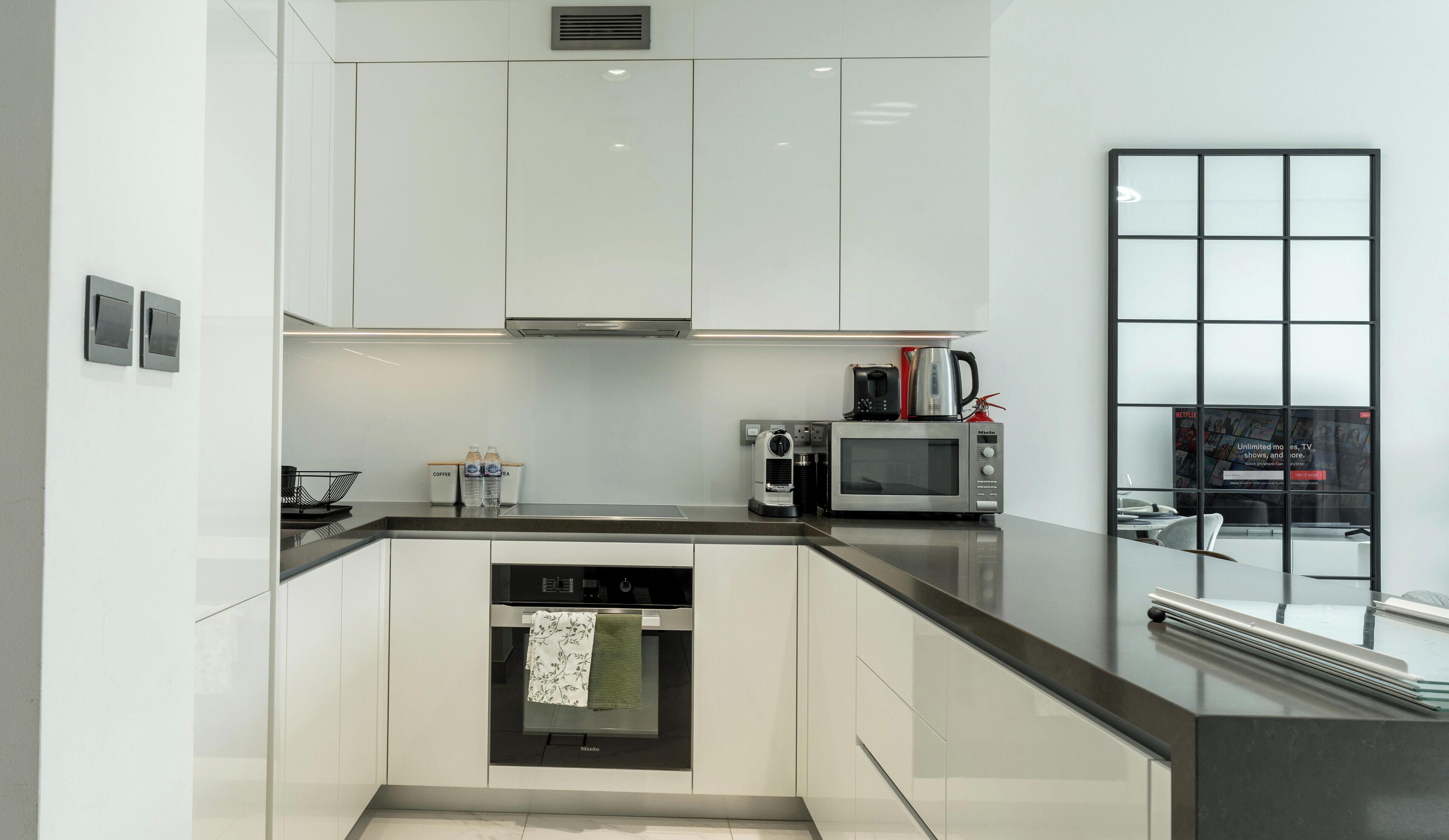 Una cocina moderna con armarios blancos, horno empotrado, microondas y cafetera.