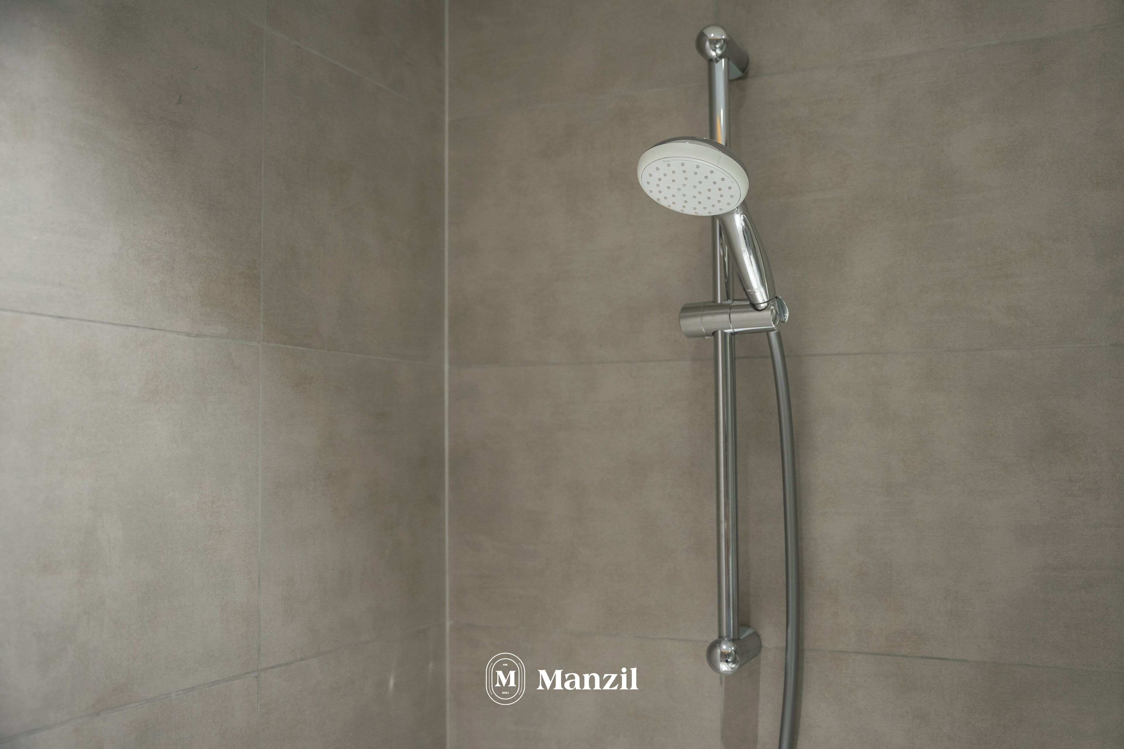 A shower with a handheld showerhead and a wall-mounted control.