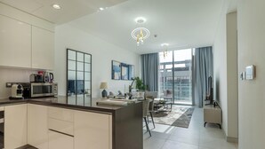 A modern kitchen with a built-in microwave and toaster, a dining area with a table and chairs, and a large window with curtains. - Manzil - Lux 1BR minutes to Dubai Mall (Dubai)