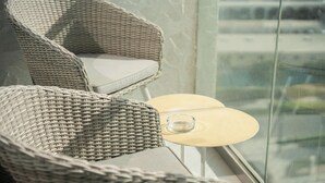 Wicker chairs with cushions, a small round table with a glass object, and a view through a window. - Manzil - Lux 1BR minutes to Dubai Mall (Dubai)