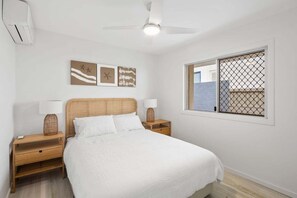 A bedroom with a bed, nightstands, a ceiling fan, artwork on the wall, and a window with a view.
