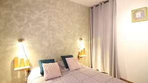 A bedroom with a bed, two bedside lamps, a wall-mounted light, and a curtain. - Beautiful F3 with parking and pets allowed, near thermal baths (Mont-Dore)