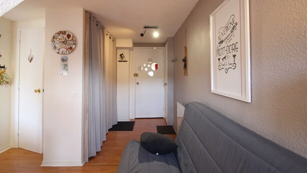 En hall med en grå soffa, en dörr med ett nummer på och en inramad affisch på väggen.