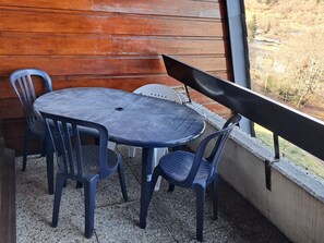 Eine kleine Außenbereich-Sitzgelegenheit mit einem runden Tisch und vier Stühlen, einer Holzwand und Blick auf eine hügelige Landschaft.