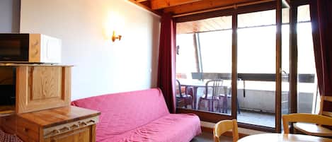 Una habitación acogedora con techo de madera, un sofá rosa, una pequeña mesa de madera y una ventana con vista a muebles de exterior.